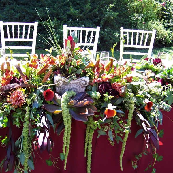 Long floral table centerpiece with burgundy, orange, and green blooms