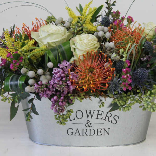 Mixed floral arrangement in a metal container with white roses and colorful blooms