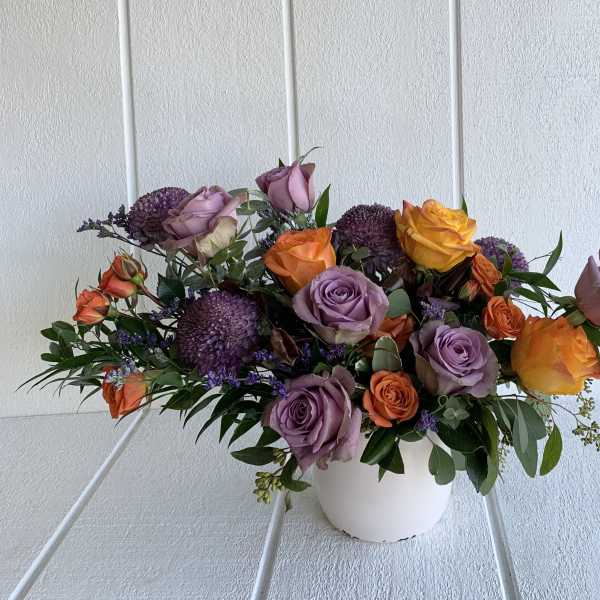 Mixed rose arrangement in a white vase with purple accents