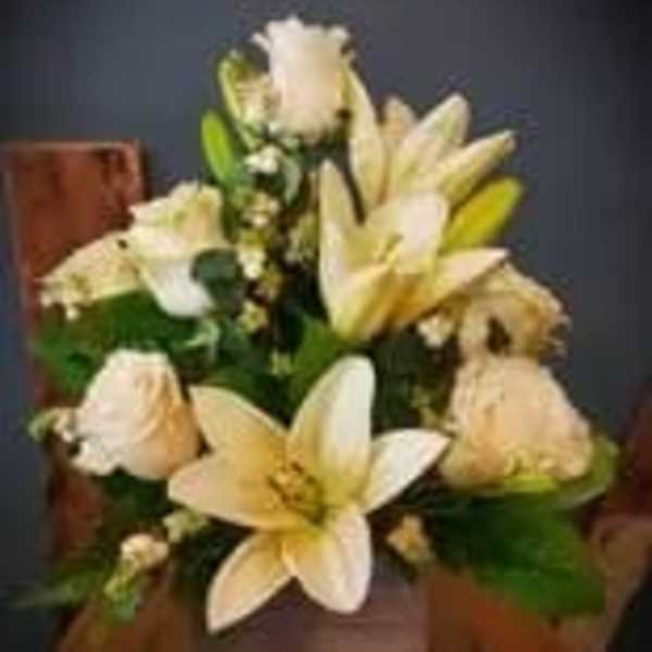 Cream lilies and roses arranged in a wooden basket