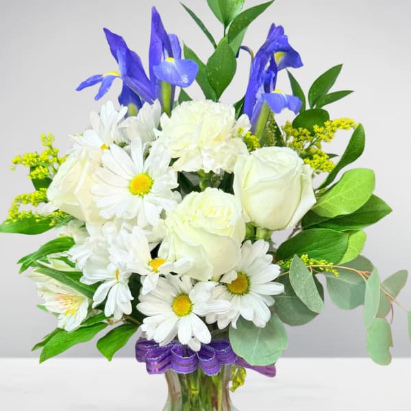 White roses and daisies with blue irises in a glass vase