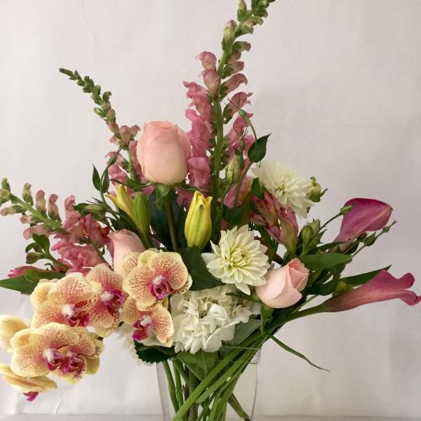 Mixed bouquet in a clear glass vase with pink roses, orchids, and white blooms