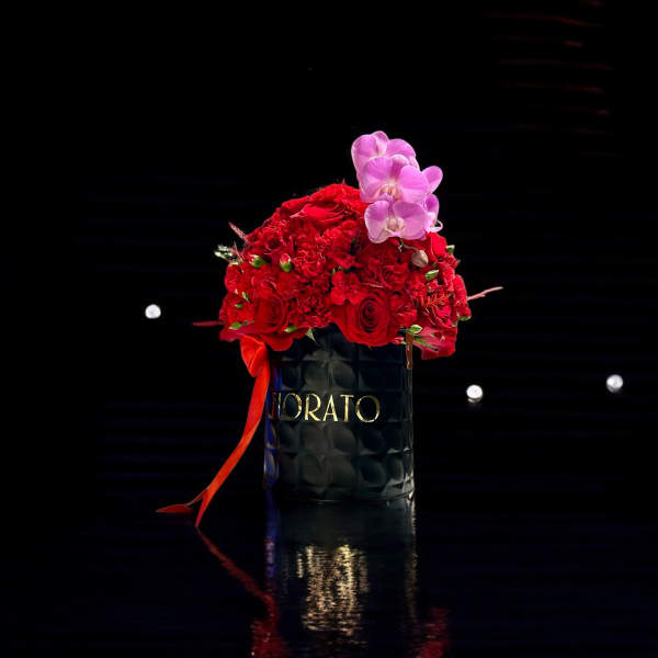 Red rose arrangement in a black container with pink orchids