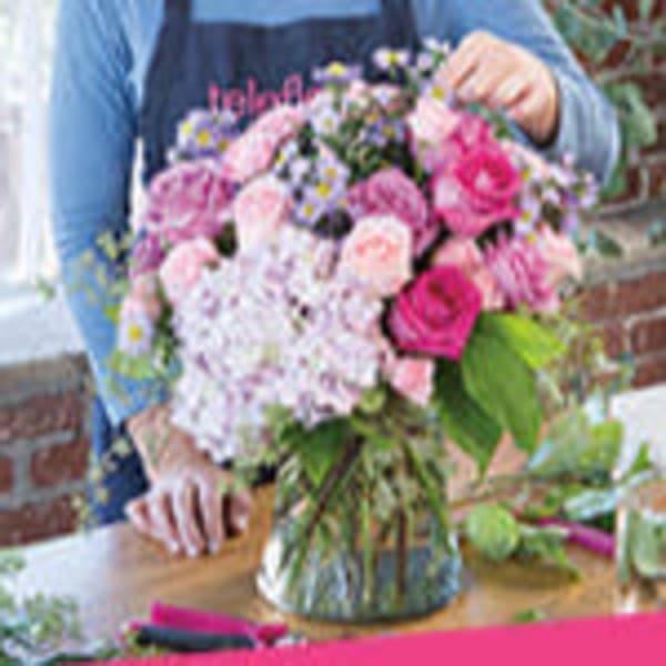 Round bouquet of pink and purple flowers in a clear glass vase on a table