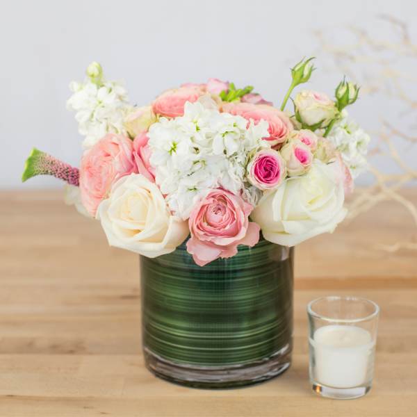 Pink and white roses in a green glass vase beside a small candle