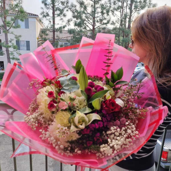 Large bouquet of mixed pink, white, and red flowers wrapped in bright pink paper