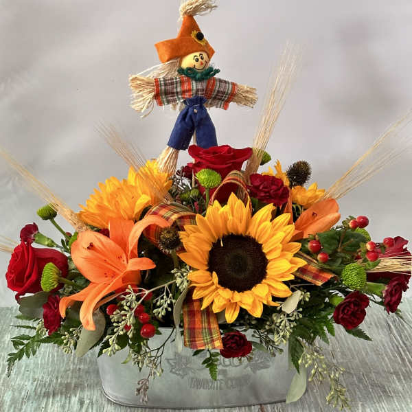 Fall floral arrangement with sunflowers, roses, and a scarecrow topper in a metal container