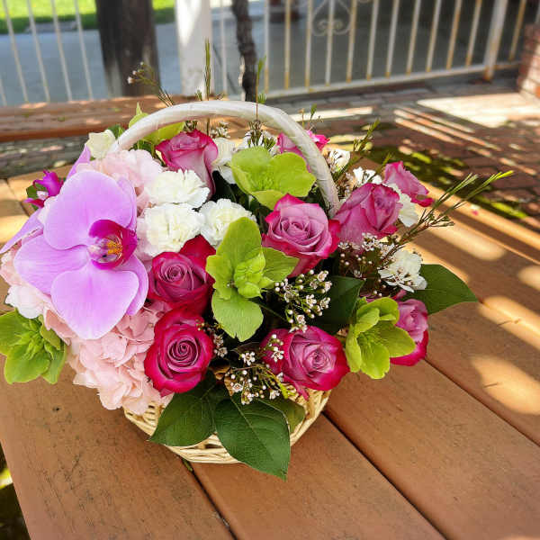 Basket arrangement of pink roses, orchids, hydrangea, and white carnations