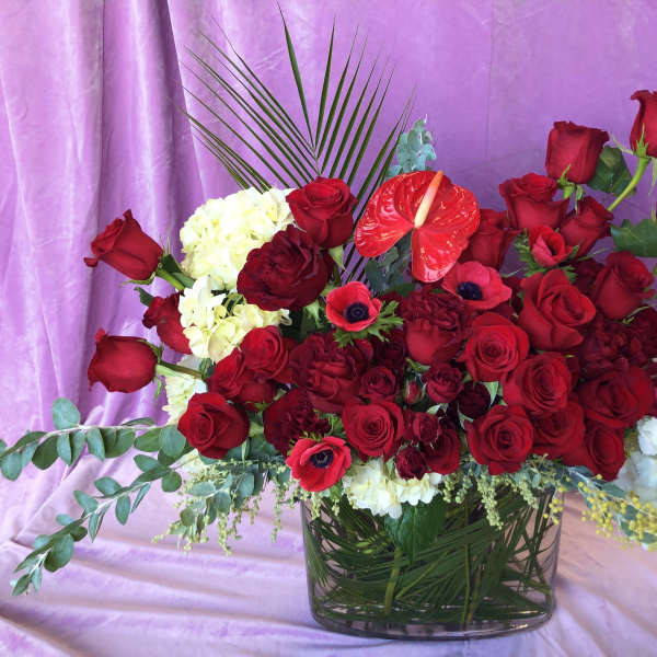 Red rose arrangement in a glass vase with white blooms and tropical accents
