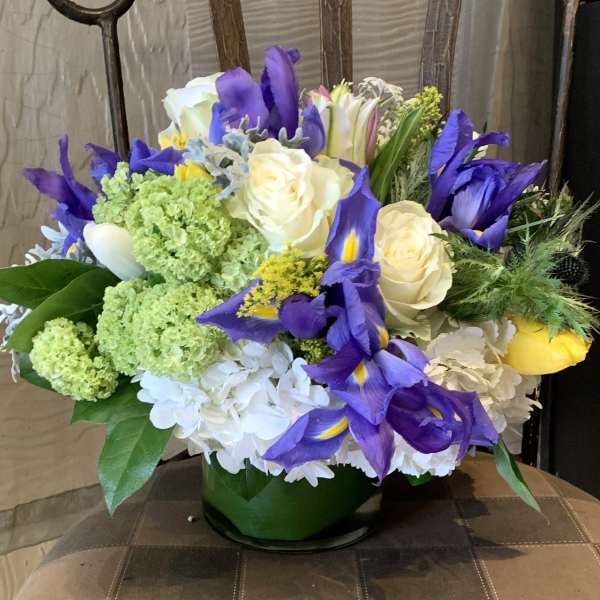 Bouquet of purple irises, white roses, and green hydrangeas in a glass vase