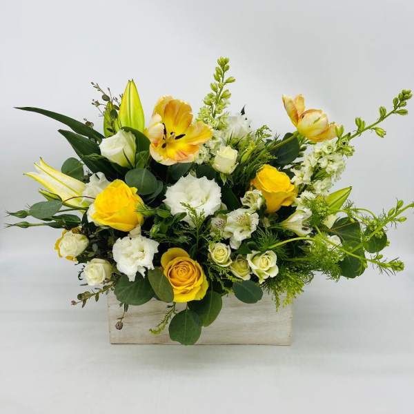 Low rectangular arrangement of yellow and white flowers in a whitewashed wooden box