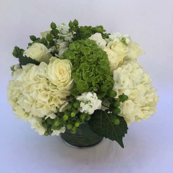 White roses and hydrangeas arranged in a glass vase with green accents