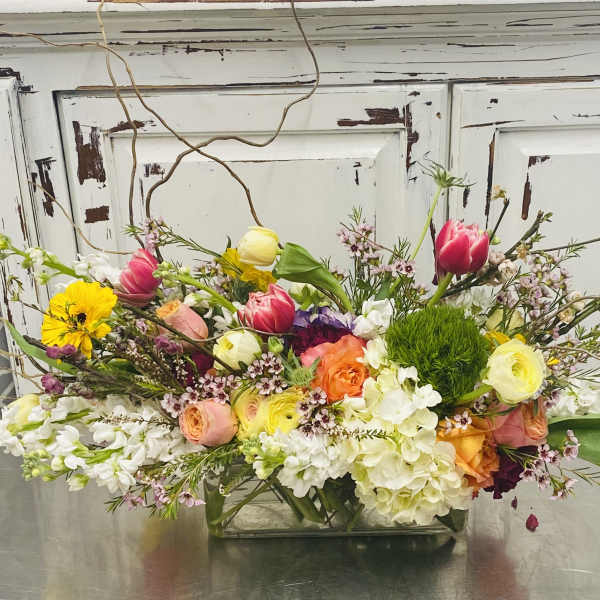 Mixed bouquet in a low rectangular glass vase with pink, yellow, white, and orange blooms