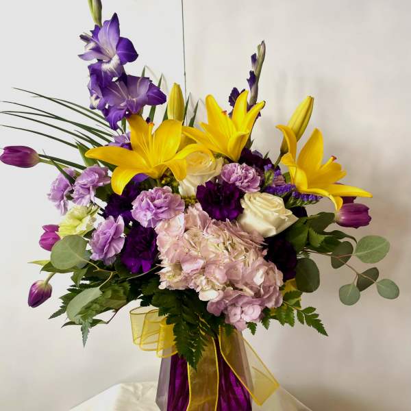 Purple and yellow floral arrangement in a purple vase with a yellow ribbon