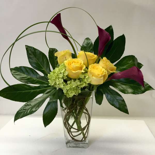 Yellow roses and purple calla lilies in a clear glass vase