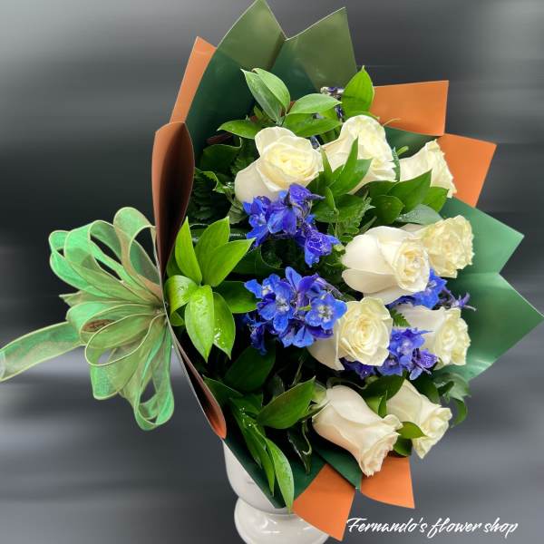 Bouquet of white roses and blue delphinium in colorful wrap with a green bow
