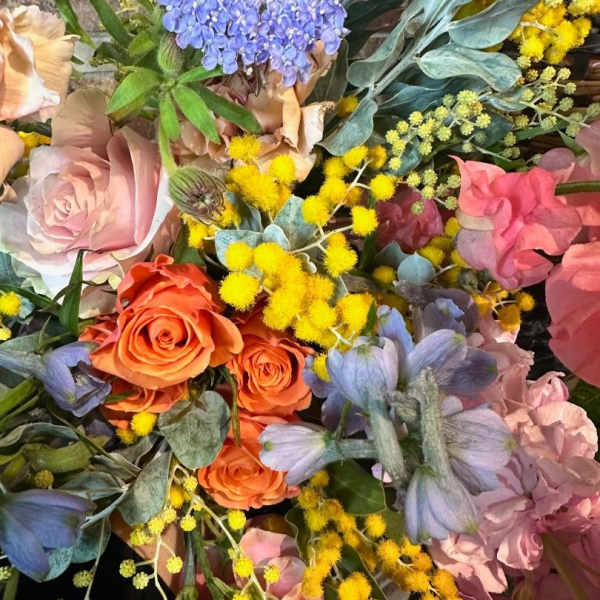 Mixed bouquet with orange and pink roses, blue flowers, and yellow filler blooms