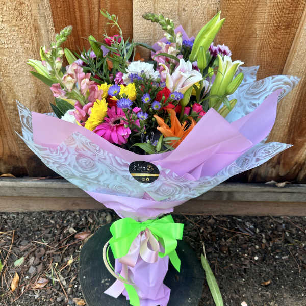 Mixed bouquet of colorful flowers wrapped in pink paper with a green ribbon