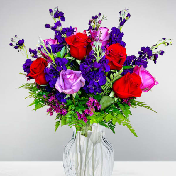 Bouquet of red, pink, and lavender roses in a clear glass vase