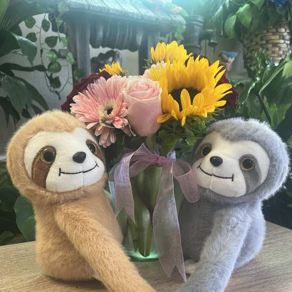 Bouquet with pink and yellow flowers in a glass vase, flanked by two plush sloths