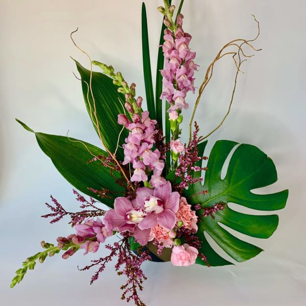 Pink orchid arrangement with tropical leaves and curly branches