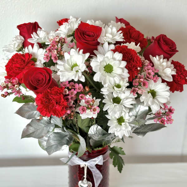 Red roses and white daisies in a red glass vase with a ribbon