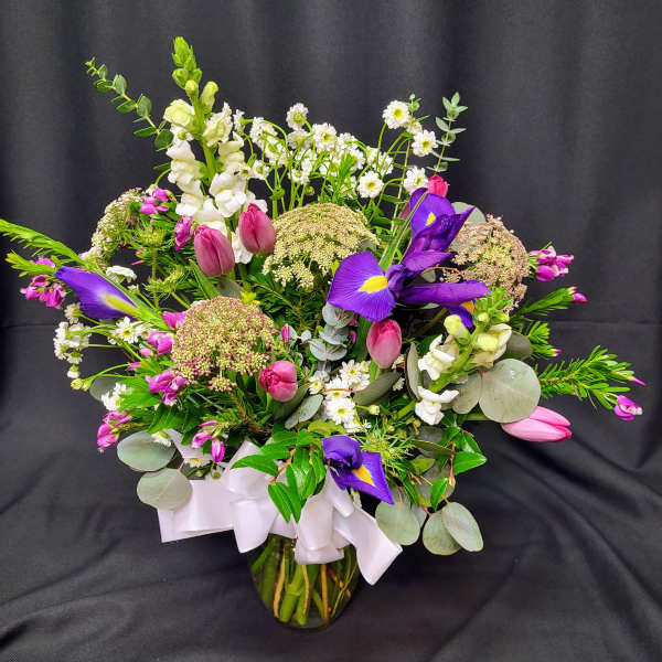 Mixed bouquet with purple irises, pink tulips, and white snapdragons in a glass vase