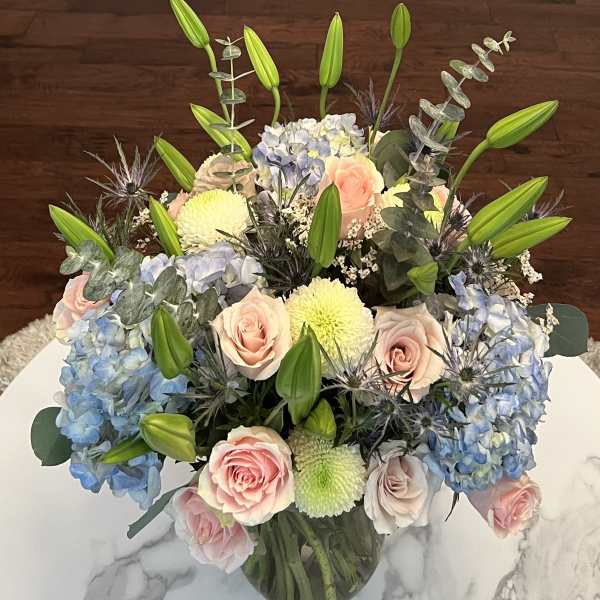 Bouquet of pastel roses, blue hydrangeas, and lilies in a glass vase