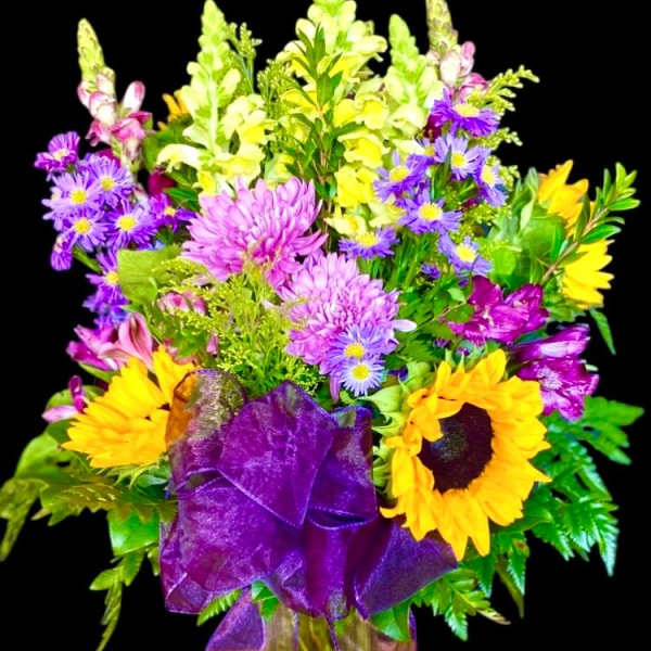 Colorful bouquet with sunflowers, purple daisies, and yellow snapdragons in a vase