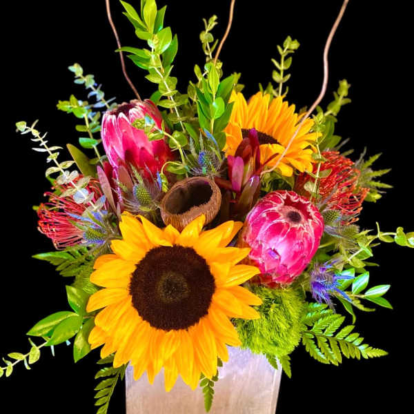 Sunflowers and pink protea in a square vase with greenery