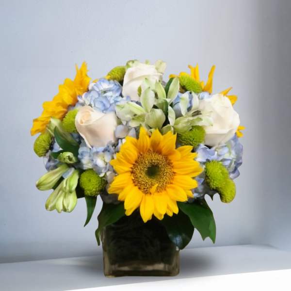 Bouquet of sunflowers, white roses, and blue hydrangeas in a glass vase
