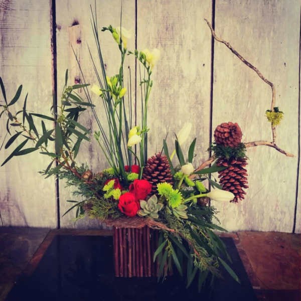 Mixed floral arrangement with red roses, white blooms, and pinecones in a rustic container