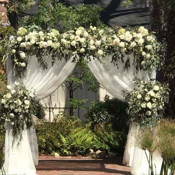 White floral wedding arch with draped fabric and greenery
