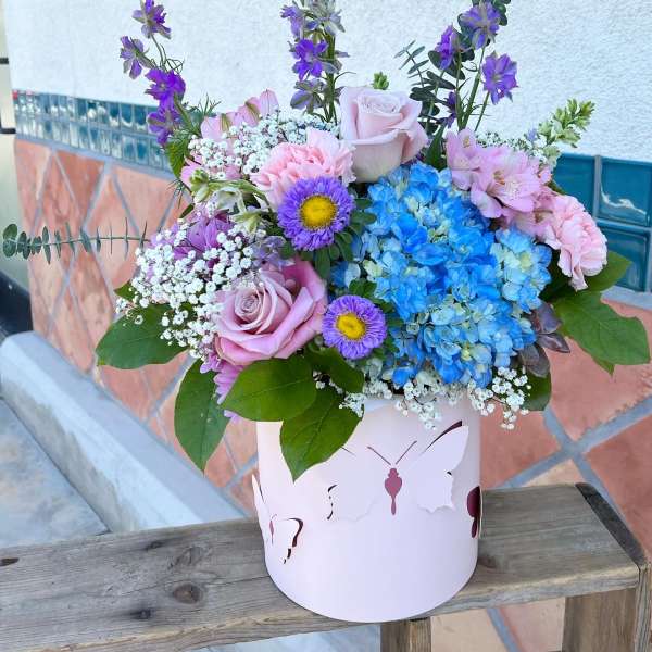 Bouquet of pink roses, blue hydrangeas, and purple flowers in a pink butterfly box