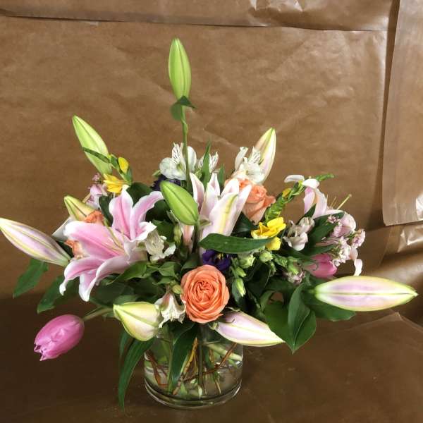 Mixed bouquet of pink lilies, orange roses, and assorted flowers in a glass vase