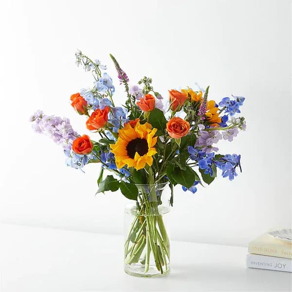 Mixed bouquet with a sunflower and orange roses in a clear glass vase