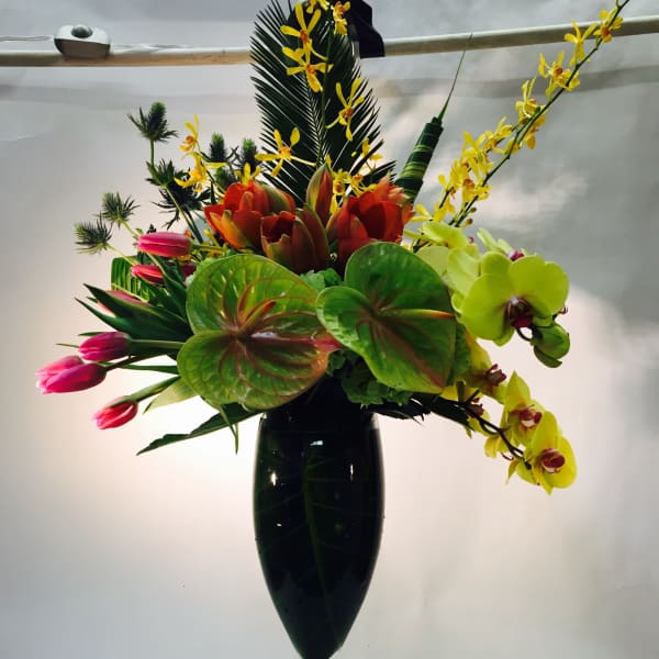 Tropical flower arrangement in a tall glass vase with orchids and tulips