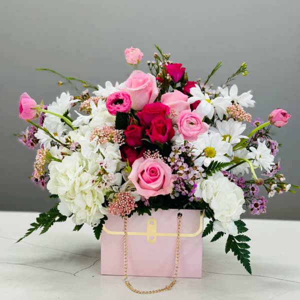 Pink and white flower arrangement in a pink gift box with a gold chain handle
