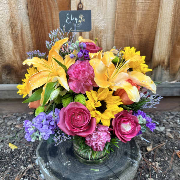 Colorful mixed bouquet in a glass vase with roses, lilies, and sunflowers