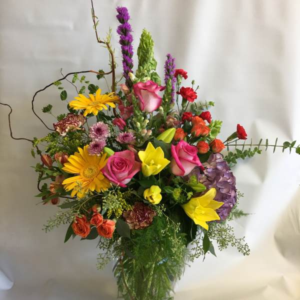 Colorful mixed bouquet in a clear glass vase with roses, lilies, and gerbera daisies