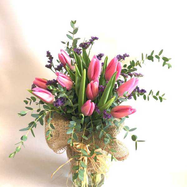 Pink tulips arranged in a burlap-wrapped vase with purple filler flowers