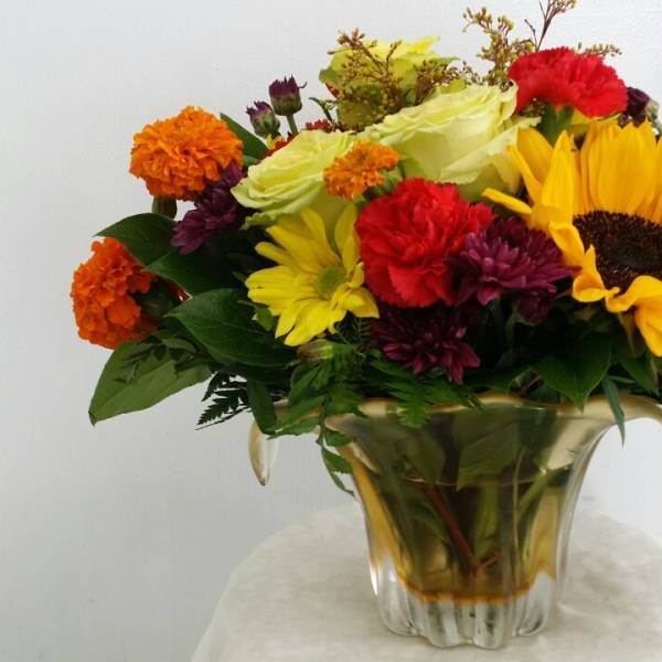 Mixed bouquet with sunflowers, roses, and carnations in a gold vase