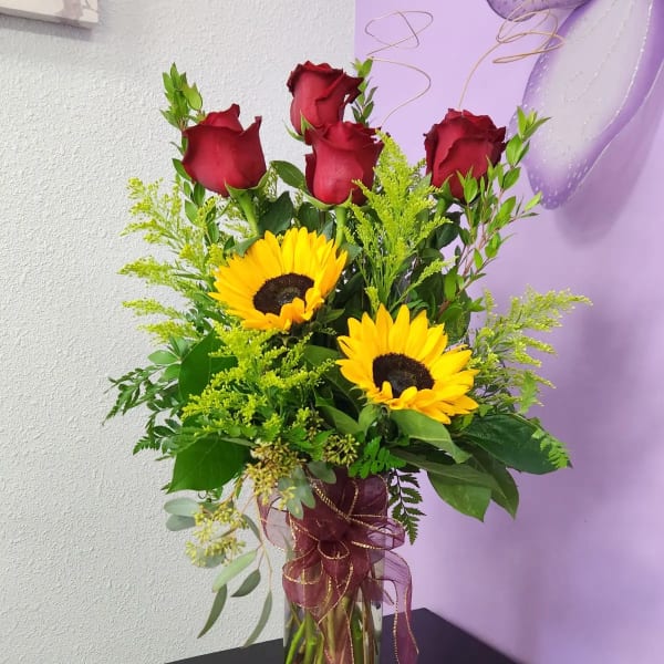 Red roses and sunflowers in a clear glass vase with ribbon