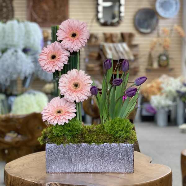 Pink gerbera daisies and purple tulips in a glittery rectangular container