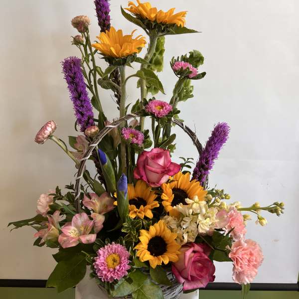 Basket arrangement with sunflowers, pink roses, and purple spikes