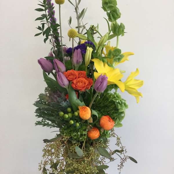 Tall mixed bouquet with yellow lilies, purple tulips, and orange roses in a glass vase