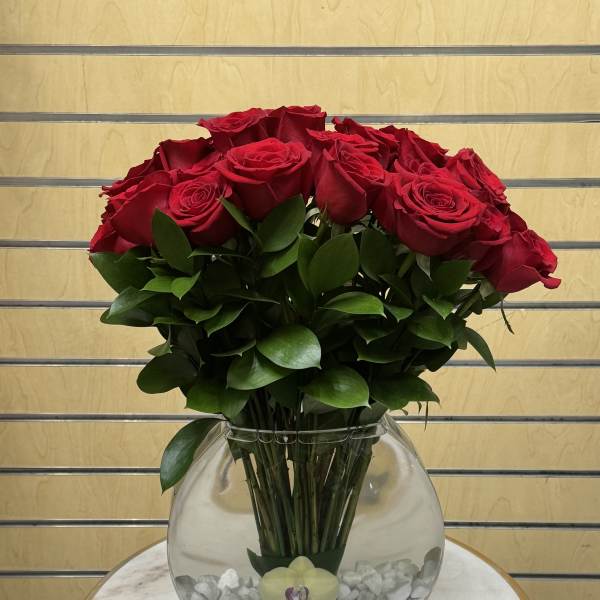 Red roses arranged in a clear round glass vase with white stones.