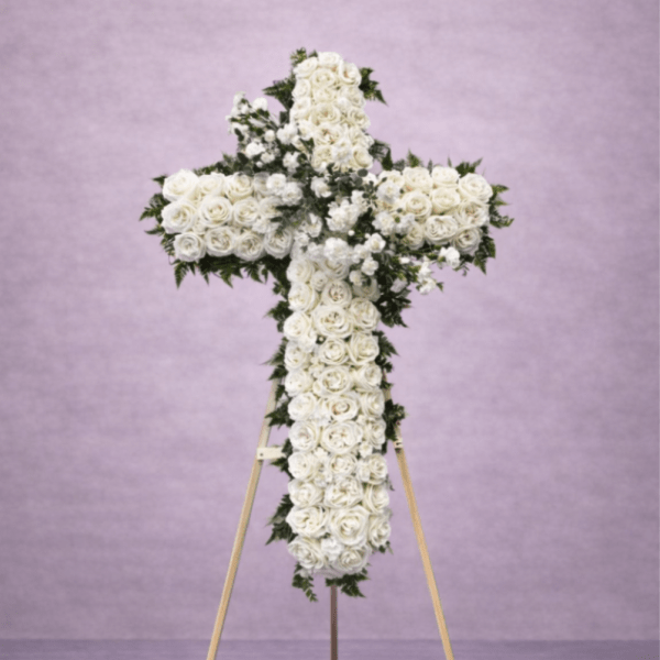 Standing cross-shaped spray of white roses on a wooden easel against a soft lavender background