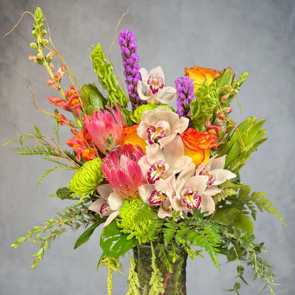 Mixed bouquet with orchids, roses, and green blooms in a glass vase