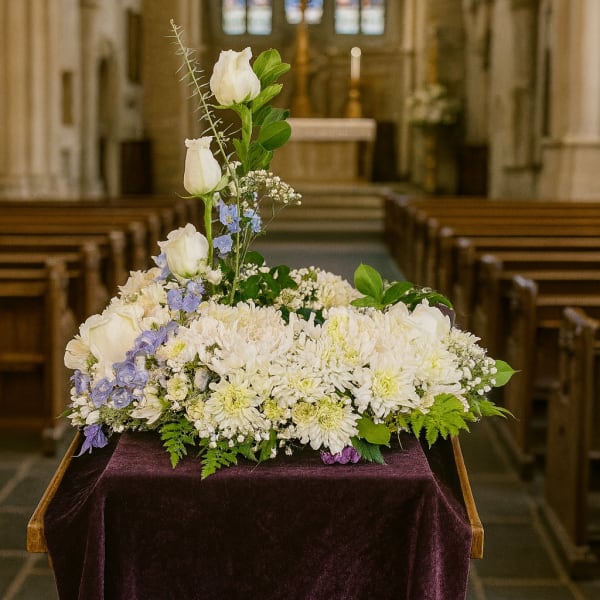 White floral arrangement with blue accents on a draped stand in a church